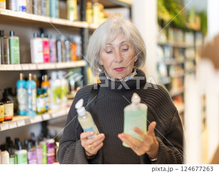 Senior woman client selects care product for problem skin, reads annotation Senior woman client selects care product for problem skin, reads annotation 124677263