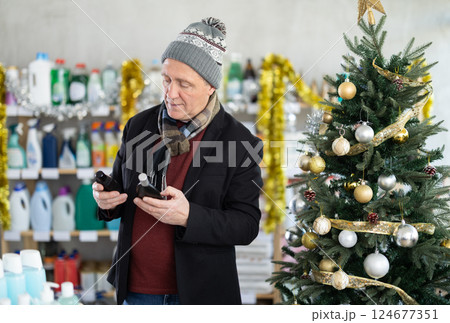 In X mas atmosphere, senior man sniffs fragrance of perfume, chooses scent spray with pleasant smell In X mas atmosphere, senior man sniffs fragrance of perfume, chooses scent spray with pleasant smell 124677351