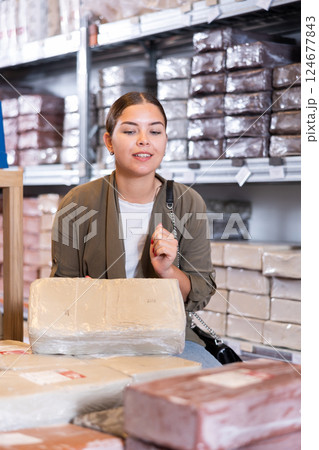 Young woman carefully chooses briquettes with white clay in specialized store 124677843