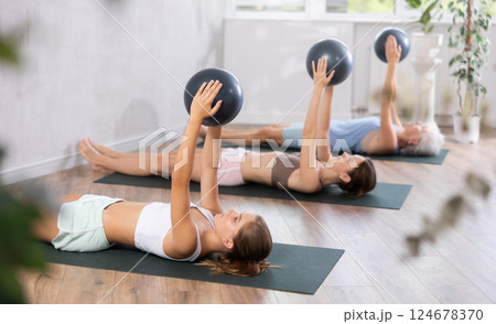 Teenage girl doing pilates with soft ball in group Teenage girl doing pilates with soft ball in group 124678370