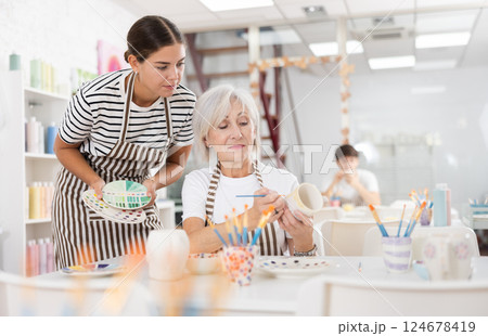 Young female instructor sharing art of ceramics painting with mature woman in pottery class 124678419