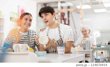 Cheerful young couple decorating ceramic pottery at table in workshop 124678454