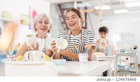 Cheerful young girl working with elderly mother in family pottery studio 124678466