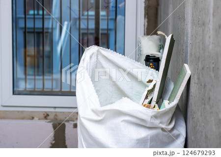 A white bag full of items is leaning against a wall A white bag full of items is leaning against a wall 124679293