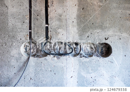 A mess of wires is suspended from an exposed concrete wall surface 124679338