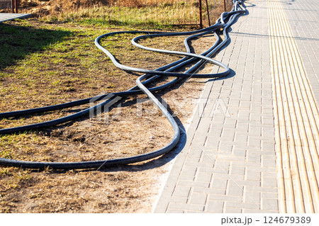 Coiled Black Hoses are Positioned Alongside a Paved Pathway in a Bustling Urban Setting Coiled Black Hoses are Positioned Alongside a Paved Pathway in a Bustling Urban Setting 124679389