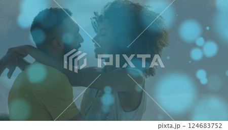Image of light spots over biracial couple embracing at seaside Image of light spots over biracial couple embracing at seaside 124683752