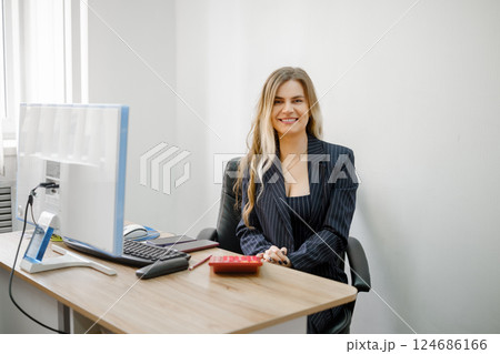 Professional woman smiling at desk with computer in modern office setting 124686166