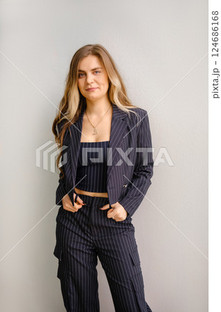 Young woman poses confidently in stylish striped suit against a neutral background 124686168
