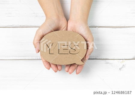 Hands Holding Cardboard 'YES' Sign Over White Wooden Background Hands Holding Cardboard 'YES' Sign Over White Wooden Background 124686187