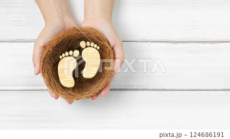 New Beginnings and Parenthood: Hands Holding Wooden Baby Footprints in a Nest New Beginnings and Parenthood: Hands Holding Wooden Baby Footprints in a Nest 124686191