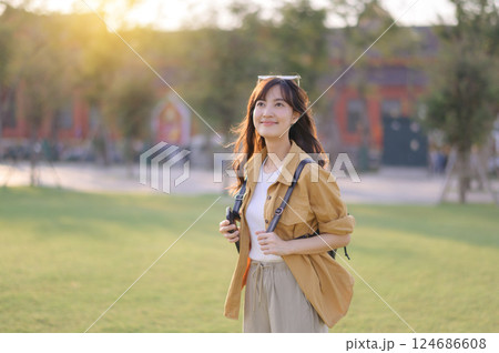 Traveler asian woman in her 30s stands bathed in the golden glow of sunset, embracing the freedom of exploration. on summer holiday weekend vacation trip in Bangkok, Thailand Traveler asian woman in her 30s stands bathed in the golden glow of sunset, embracing the freedom of exploration. on summer holiday weekend vacation trip in Bangkok, Thailand 124686608