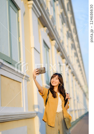 Traveler asian woman in her 30s making a livestream and selfie with a smartphone enjoying travel in Bangkok, Thailand. Journey trip lifestyle, world travel explorer or Asia summer tourism concept. 124686630