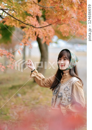 Asian woman in casual dress embraces the fall beauty of Japan, enjoying a holiday filled with smiles, fashion, and vibrant foliage. A cheerful portrait capturing the essence of a vacation. 124686659