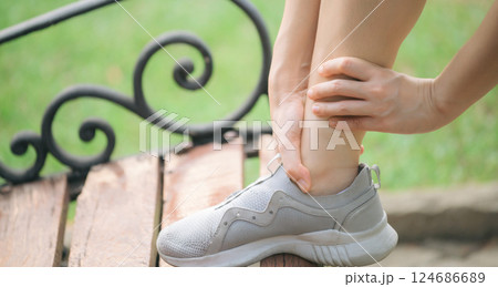 Sprained ankle problem. woman jogger. 30s asian female wearing sportswear holding her ankle with pain after running exercise in public park. 124686689