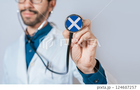 Doctor holding stethoscope with Scotland flag. Scotland health and care concept, Scotland flag on stethoscope Doctor holding stethoscope with Scotland flag. Scotland health and care concept, Scotland flag on stethoscope 124687257