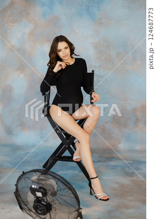 Pregnant woman in black dress sitting on a director's chair against a textured blue and brown background, expressing calm and anticipation 124687773
