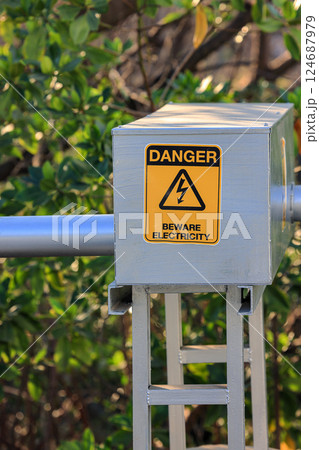 Danger beware electricity sign, Electrical Hazard High Voltage sign on metal box and tube, black triangle over yellow sign. 124687979