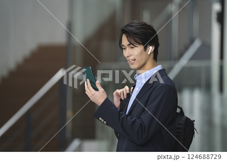 スマホの画面を見ながら話すイヤホンをした若いビジネスマン スマホの画面を見ながら話すイヤホンをした若いビジネスマン 124688729