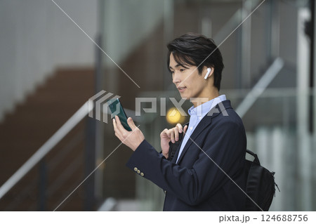 スマホの画面を見るイヤホンをした若いビジネスマン スマホの画面を見るイヤホンをした若いビジネスマン 124688756