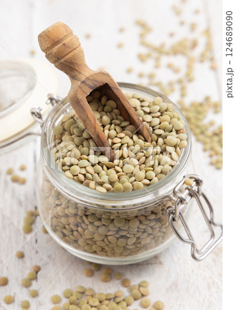 Glass jar full of raw green lentils with a wooden scoop on white table closeup. Dried legumes Glass jar full of raw green lentils with a wooden scoop on white table closeup. Dried legumes 124689090