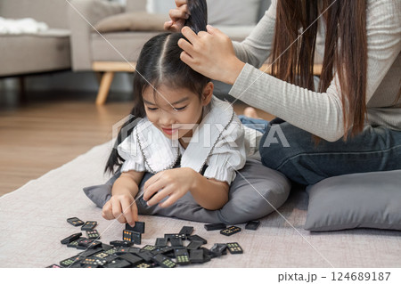 Creative Play and Hair Styling. A loving mother teaches her daughter how to style her hair while playing with dominoes. 124689187