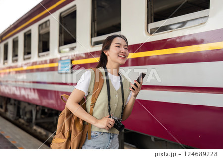 Travel Happiness and Connectivity. A young woman smiling and using her phone next to a train, blending joy with her travel experience. 124689228