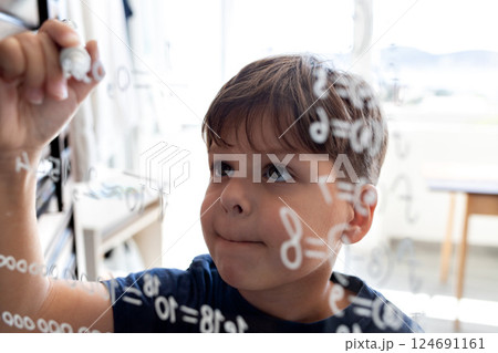 The child writes mathematical formulas on the glass with a marker. The child writes mathematical formulas on the glass with a marker. 124691161
