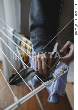 A person is actively hanging laundry on a clothes drying rack that is set up indoors 124691241