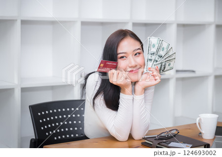 Smiling pretty woman holding credit card and US dollar. Online shopping, e-commerce, internet banking, spending money, working from home concept. 124693002