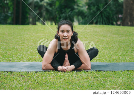 Asian woman practicing yoga on mat in outdoor park. 124693009