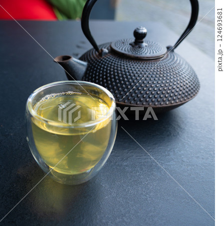 Glass cup with green tea and cast iron teapot on dark table, double wall glass 124693681