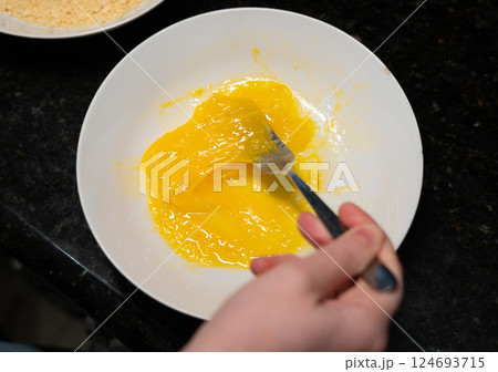 Female hands beat eggs with fork in a bowl, homemade schnitzel cooking process closeup Female hands beat eggs with fork in a bowl, homemade schnitzel cooking process closeup 124693715