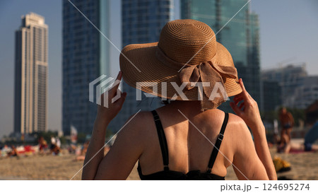 Woman in black bikini on beach holding hat with hands from strong wind 124695274