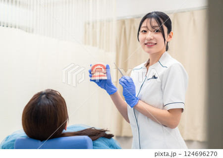 歯の模型を使って患者に説明をする歯科助手の女性 124696270