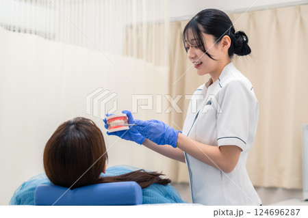 歯の模型を使って患者に説明をする歯科助手の女性 124696287
