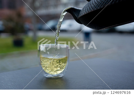 Pouring green tea into a glass from a metal kettle on blurred background, hot drink in teapot 124697616