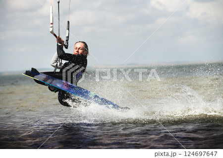 A view through a telephoto lens of a kitesurfer doing a trick with a darkslide. Focus on the splashes. The athlete is out of focus 124697647