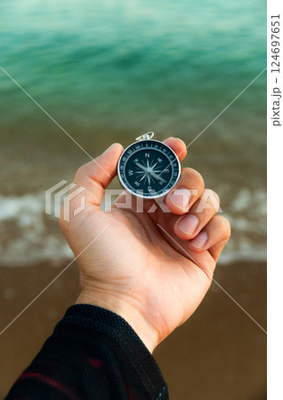 Pov of man hand holding navigational travel compass to find direction and next destination place. Concept of travel people and exploring. Beach and ocean in background 124697651