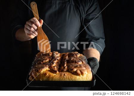 A chef wearing a black apron holds a tray of freshly baked bread with intricate designs A chef wearing a black apron holds a tray of freshly baked bread with intricate designs 124698142