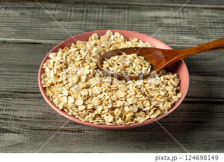 A bowl filled with rolled oats sits on a rustic wooden surface. A wooden spoon rests partially in the oats, suggesting readiness for cooking or preparing a wholesome breakfast A bowl filled with rolled oats sits on a rustic wooden surface. A wooden spoon rests partially in the oats, suggesting readiness for cooking or preparing a wholesome breakfast 124698149