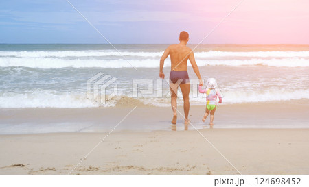 Tanned sporty man leads cute toddler girl to swim in ocean waves Tanned sporty man leads cute toddler girl to swim in ocean waves 124698452