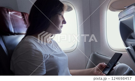 Woman using smartphone while looking out airplane window during flight 124698457