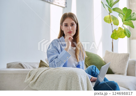 Portrait of young beautiful smiling blonde woman with laptop sitting on sofa at home 124698817