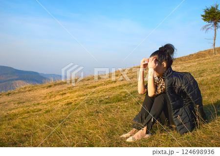 Young sad woman sitting on a mountainside Young sad woman sitting on a mountainside 124698936