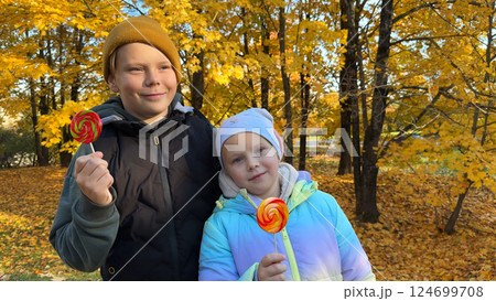 Portrait of a boy and a girl eating lollipops in an autumn park. 124699708