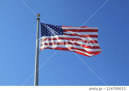 American flag flying proudly against a clear blue sky, with its red and white stripes and stars visible as it ripples in the breeze 124700015
