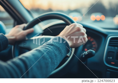Close-up of hands gripping a steering wheel inside a car at dusk, with blurred city lights visible through the windshield 124700023