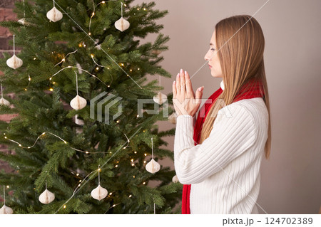 Caucasian young female in festive scene praying by christmas tree Caucasian young female in festive scene praying by christmas tree 124702389