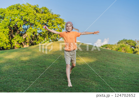 Boy wearing a pilot hat running through the grass with a toy airplane, dreaming of adventures. Childhood, imagination, and freedom concept 124702652
